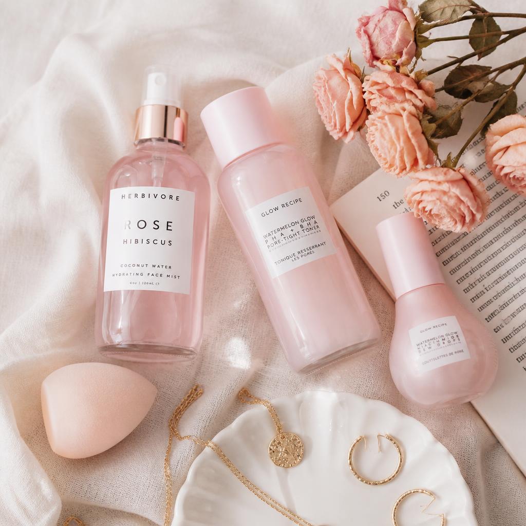 Flat lay of pink skincare bottles, jewellery and dried roses on cream linen